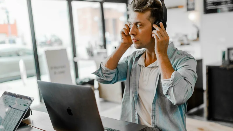 Mann mit Kopfhörern am MacBook im modernen Büro — Multi-Faktor-Authentifizierung im Unternehmen