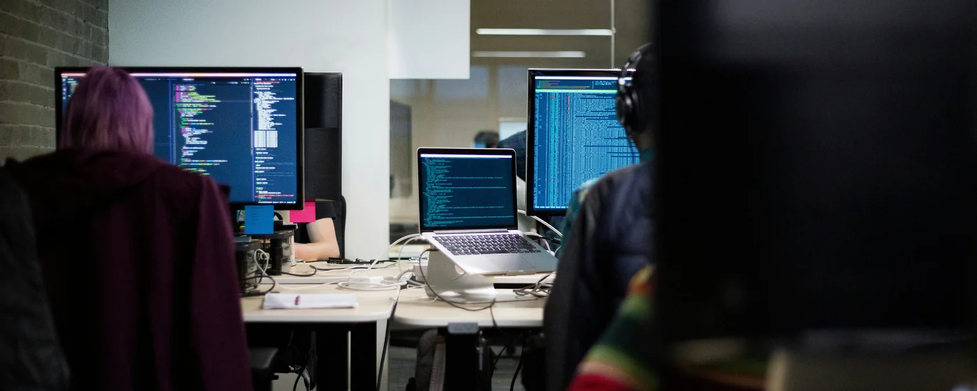 Entwicklerinnen und Entwickler von hinten an Code-Monitoren in einem modernen Büro — Das Team der Koreva eG